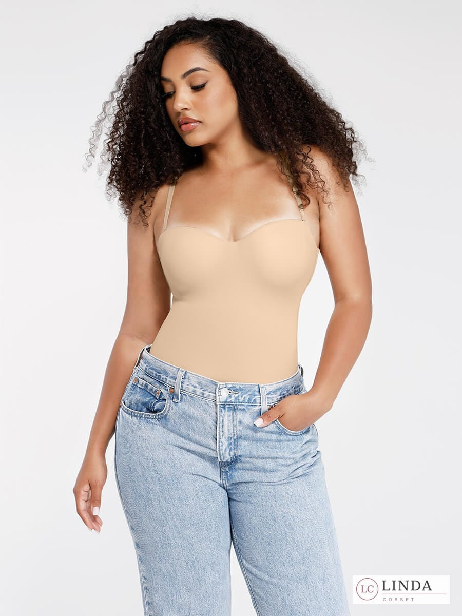 Woman wearing a beige bodysuit and light blue jeans against a white background